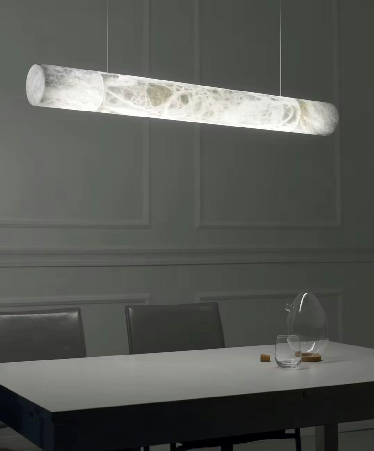 Lampada a sospensione cilindrica illumina un tavolo da pranzo con una caraffa.