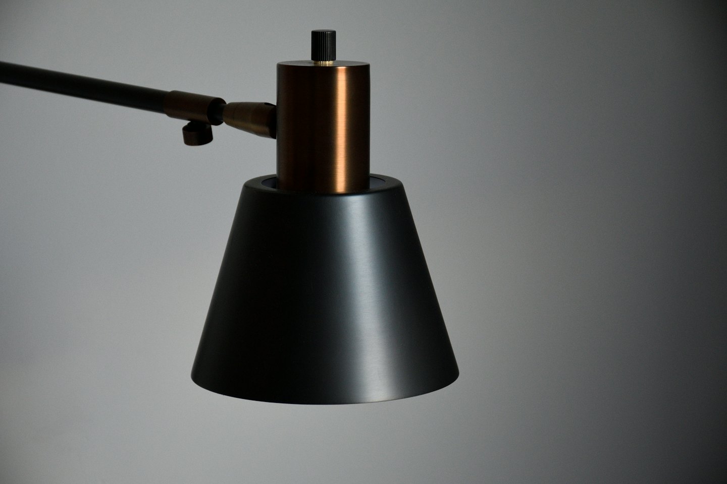 Lampada da scrivania moderna con paralume nero e snodo in rame.